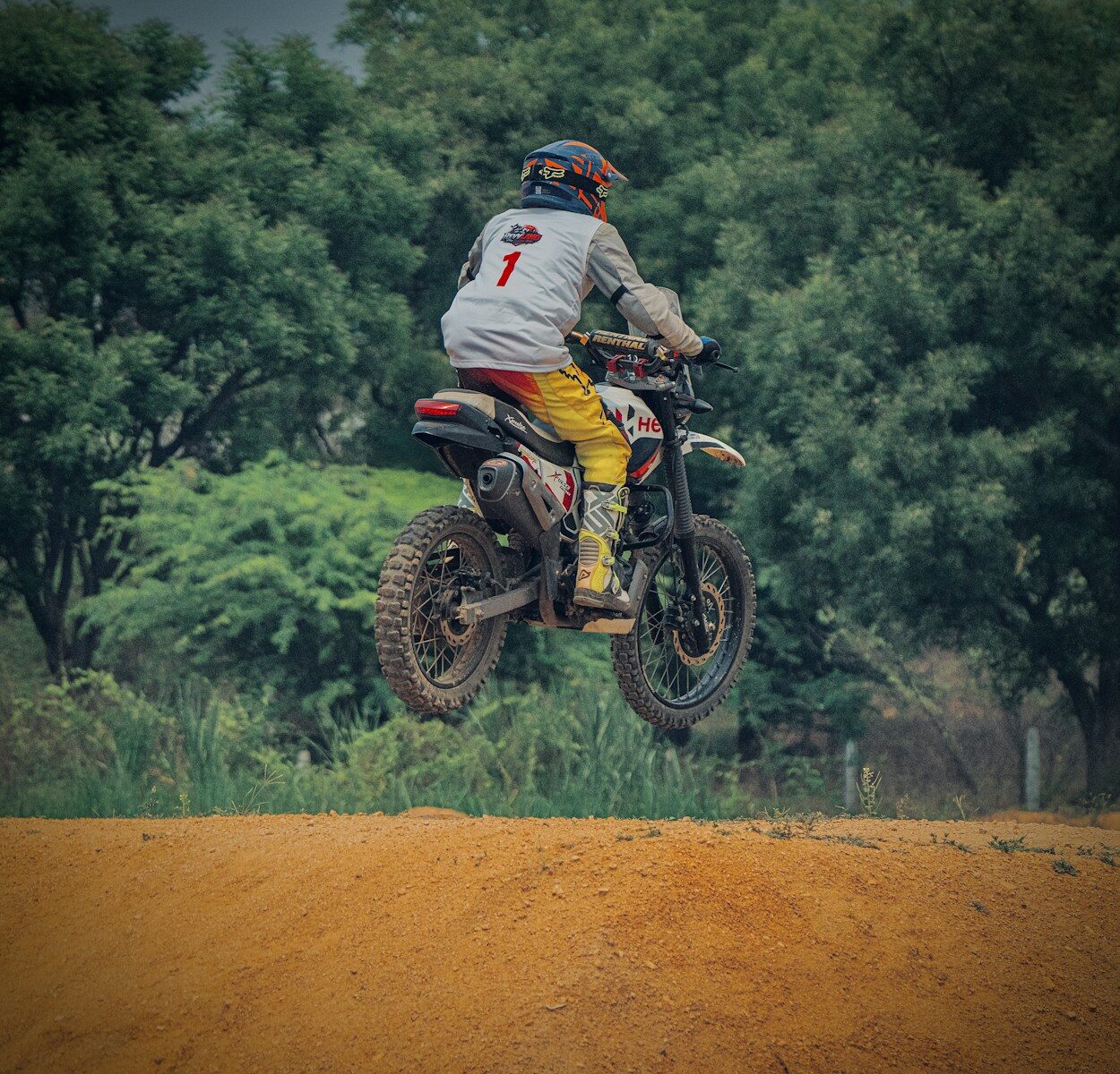 Motocross rider jumps over dirt ramp with trees background